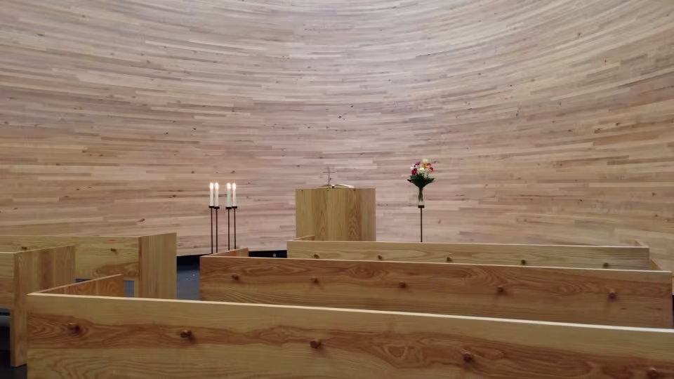 Inside the Kamppi Chapel of Silence, there is a warm, peaceful atmosphere with wooden benches, four burning candles, and a simple altar with a floral arrangement.